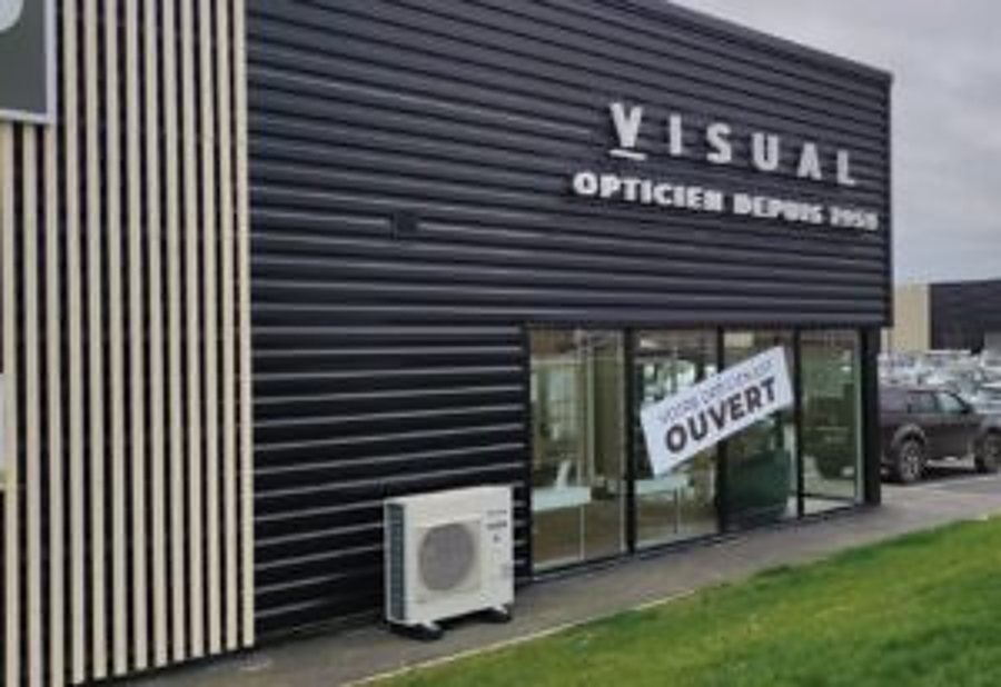 Façade moderne en bardage noir et bois d'un magasin d'optique Visual, avec une pancarte Ouvert sur la vitrine et une unité extérieure de climatisation au pied du mur.